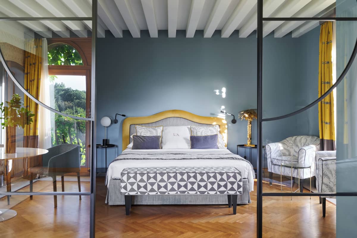 A modern bedroom with a large bed, bedside tables, a chair, and a glass partition.