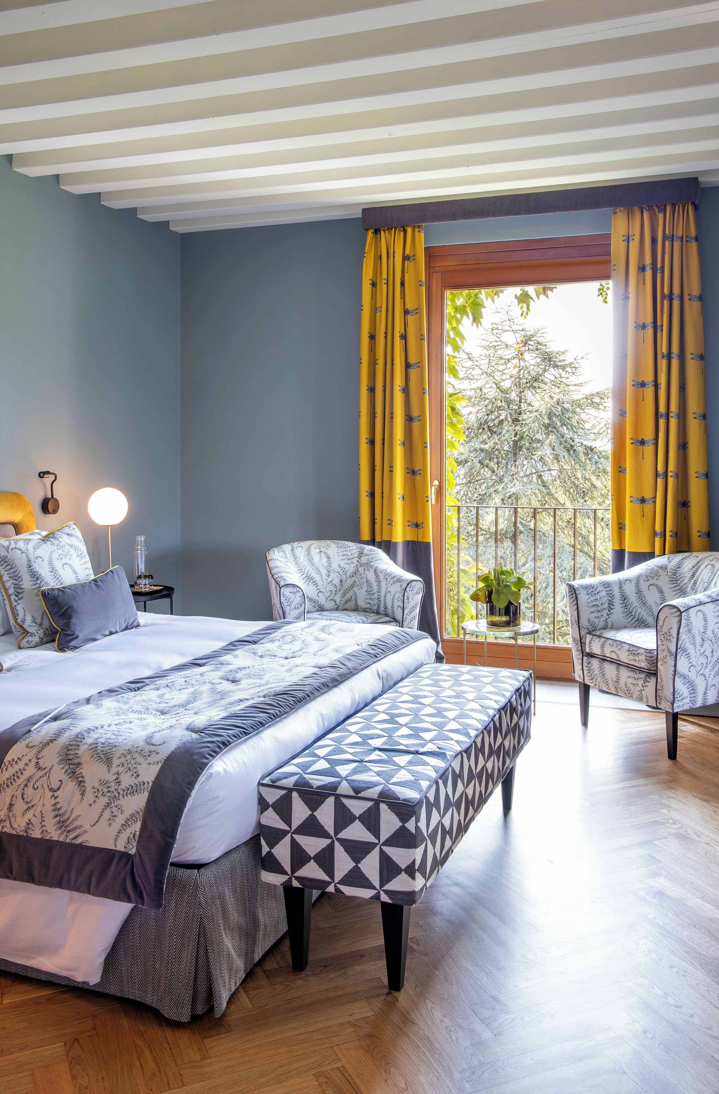 Una camera da letto con un letto, due poltrone, un comodino con una lampada e una finestra con tende.