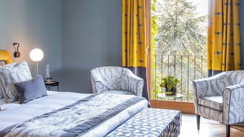 Una camera da letto con un letto, due poltrone, un comodino con una lampada e una finestra con tende.