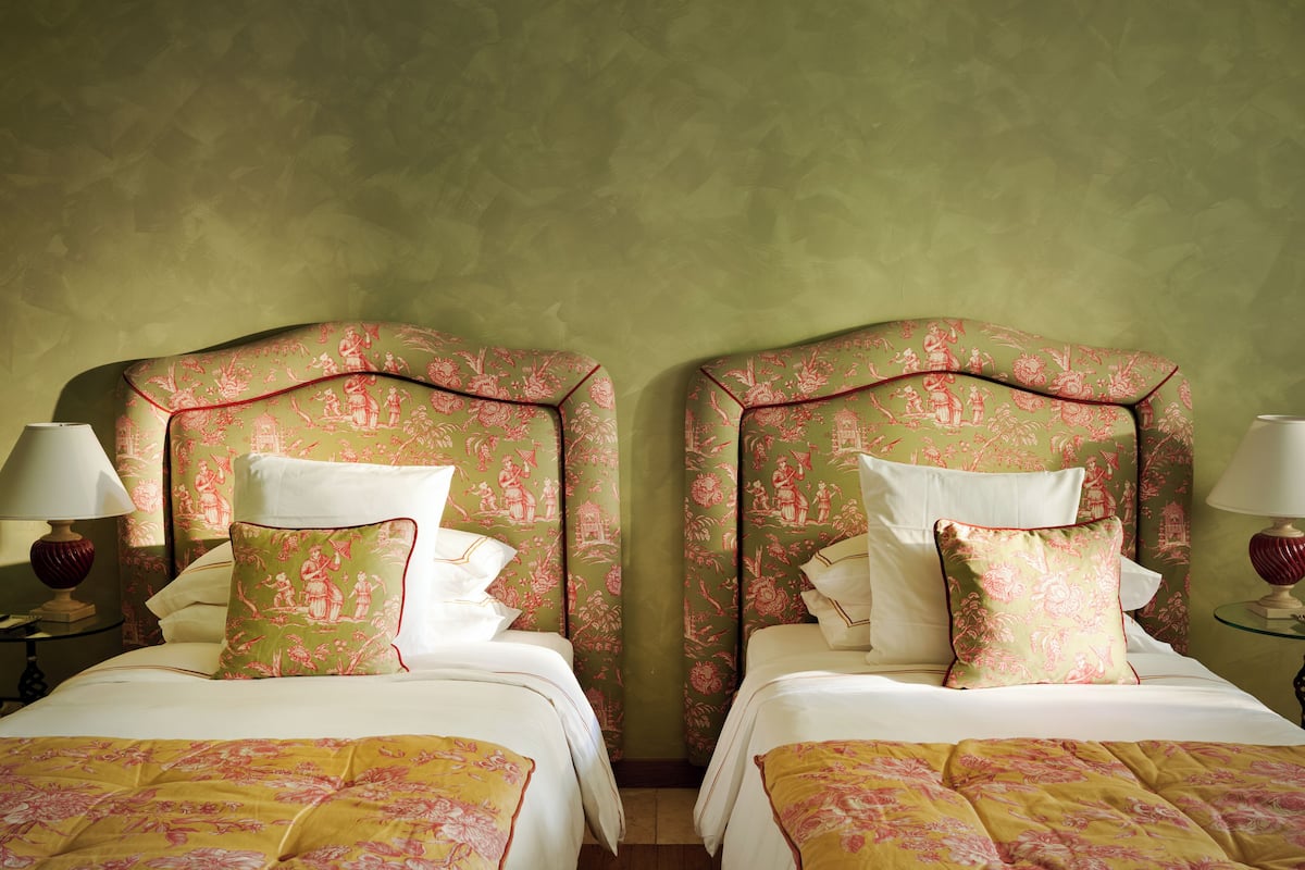 A hotel room with two beds, each with floral-patterned headboards and matching pillows.