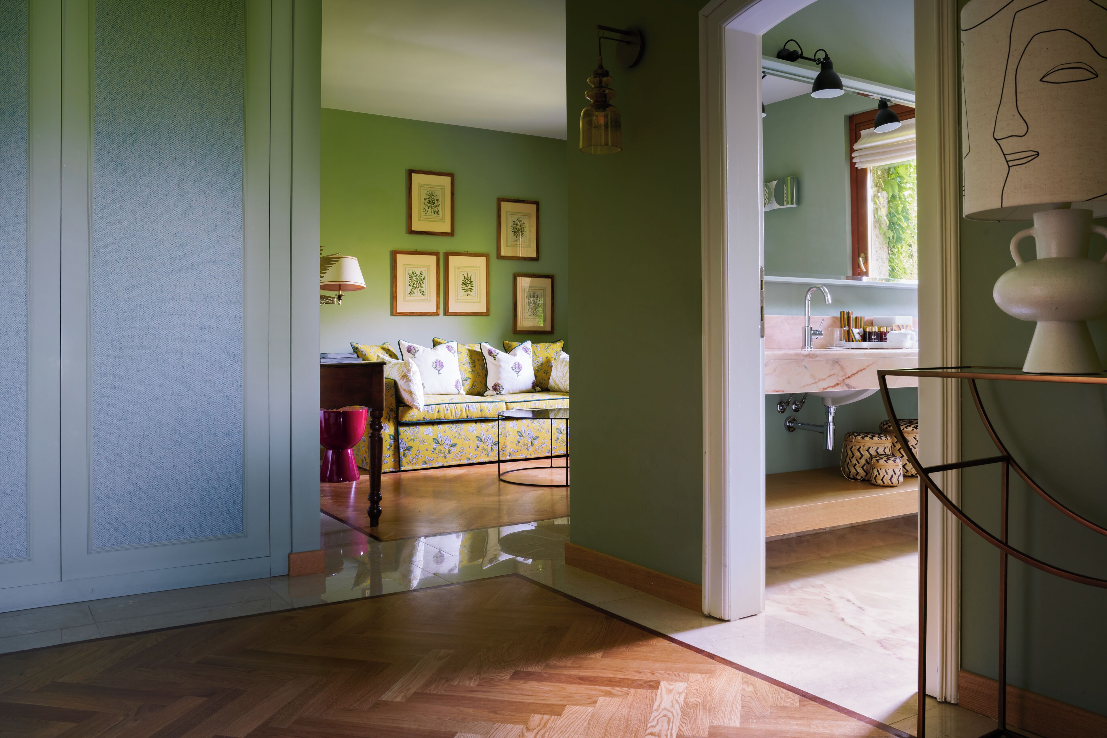 Una habitación con piso de madera, un sofá con cojines estampados, una mesita y una pared decorada con reproducciones botánicas enmarcadas.