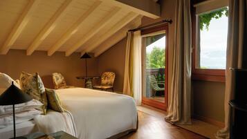 A bedroom with a large bed, a nightstand, a lamp, a chair, and a view of greenery through a window.