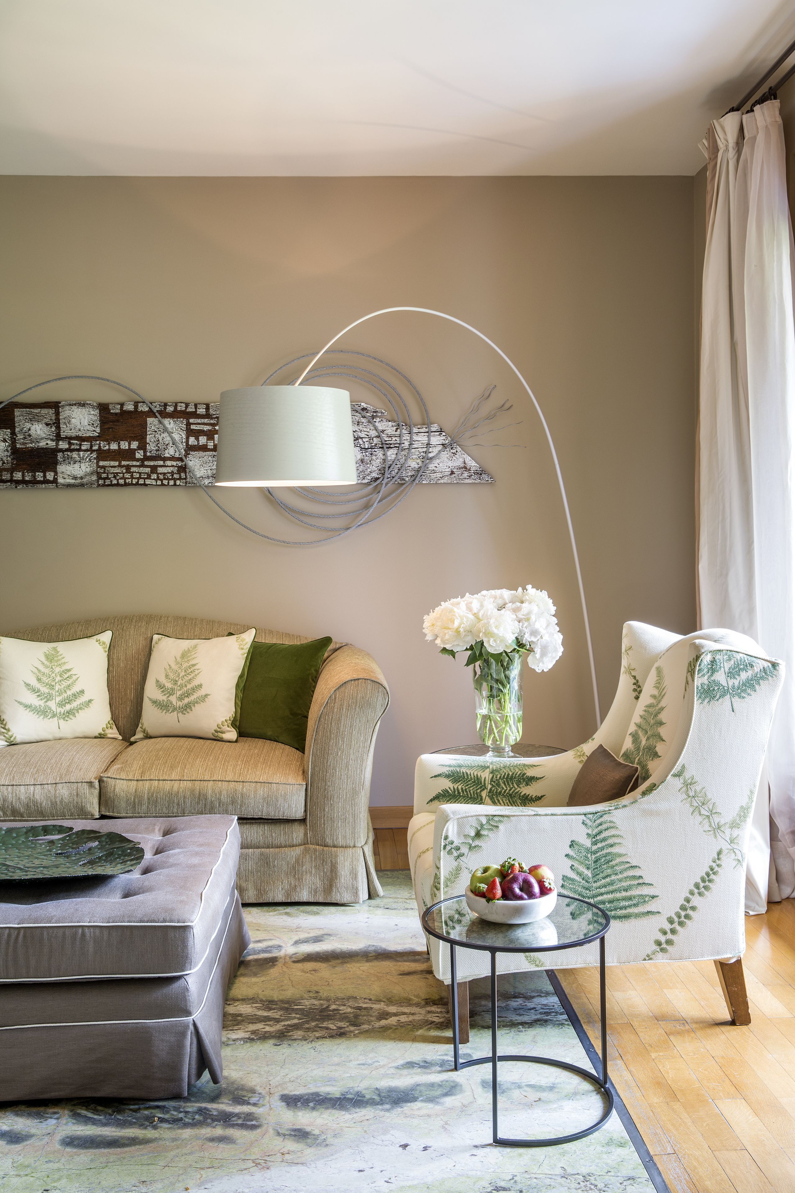 Una sala de estar con un sofá, un sillón, un reposapiés y una mesita con un jarrón de flores.