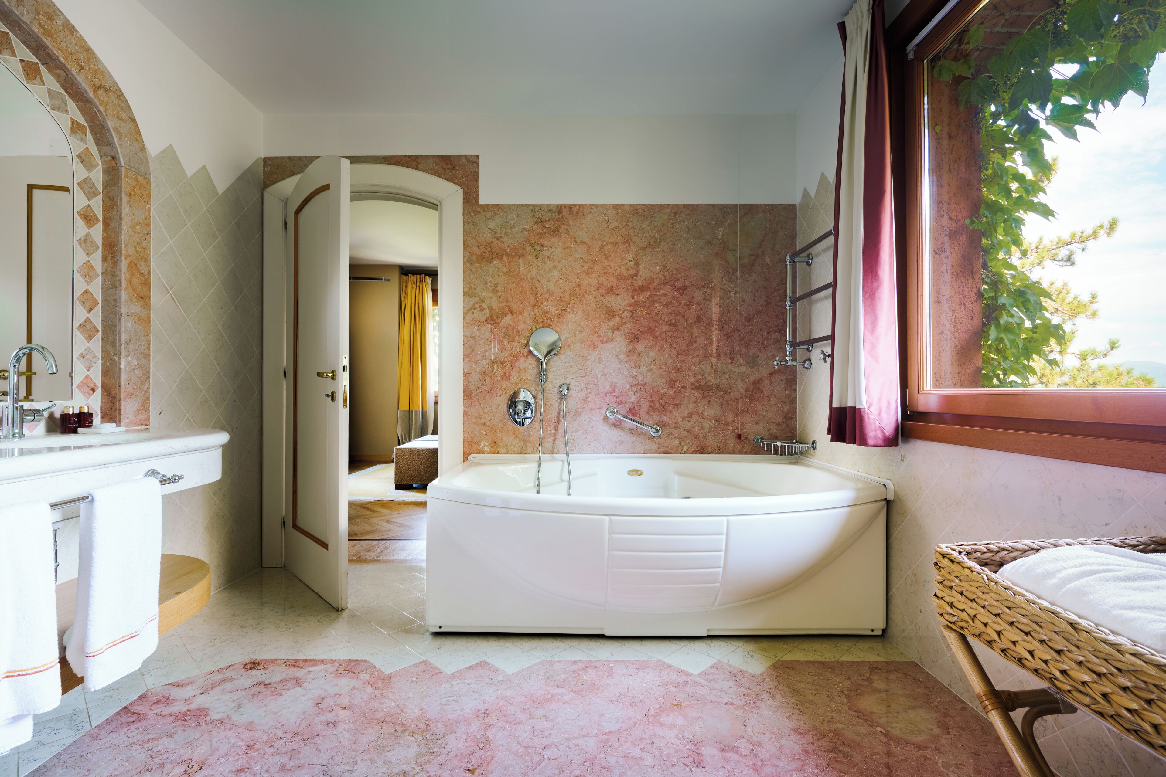 Une salle de bain avec une baignoire, un lavabo et une fenêtre donnant sur les arbres.