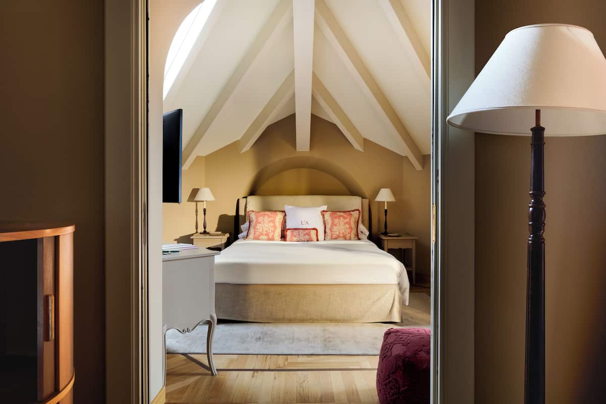 A bedroom with a large bed, two bedside tables with lamps, a wooden headboard, and a view of the sky through a skylight.