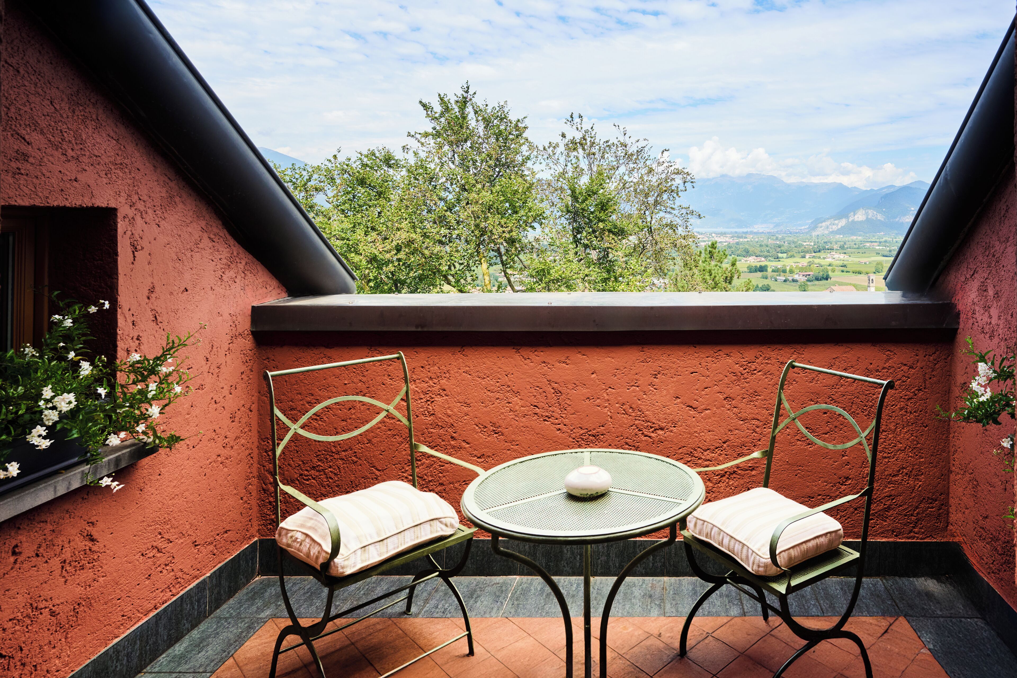 Ein Balkon mit zwei Stühlen und einem Tisch, der einen schönen Ausblick auf eine Landschaft mit Bäumen und Bergen bietet.