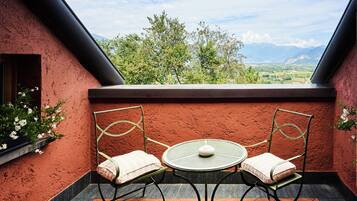 Ein Balkon mit zwei Stühlen und einem Tisch, der einen schönen Ausblick auf eine Landschaft mit Bäumen und Bergen bietet.