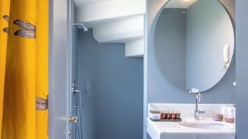 Une salle de bain avec un carrelage à motifs géométriques, un miroir rond, un lavabo blanc et un rideau jaune.