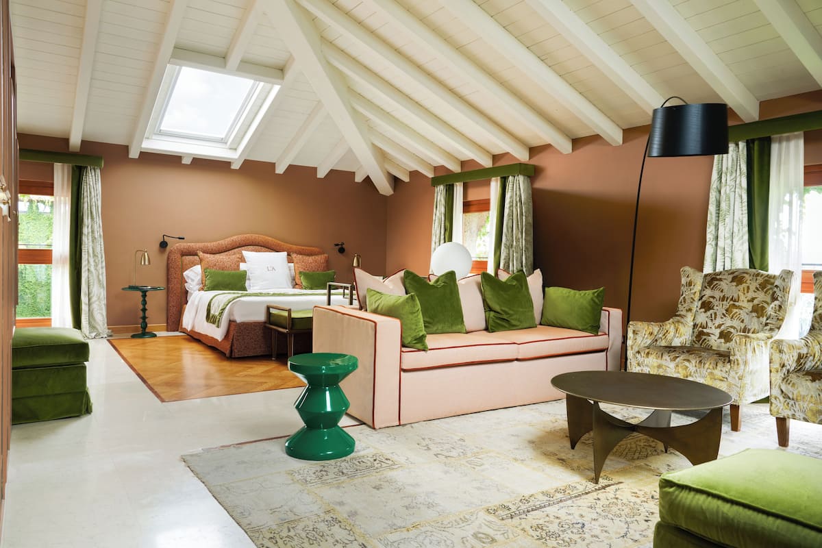 A bedroom with a bed, a sofa, a chair, a lamp, and a window with curtains.
