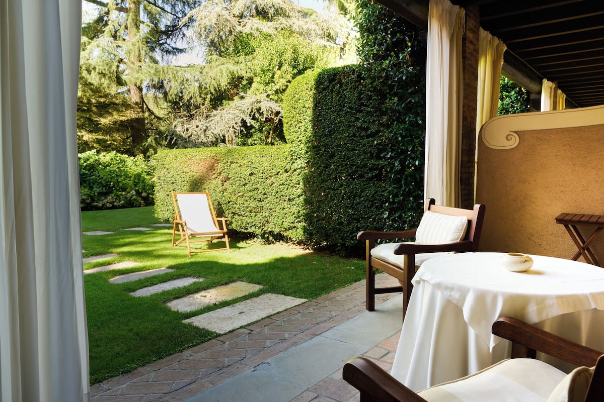 A patio with a table and chairs, a garden with a hedge, and a stone pathway.