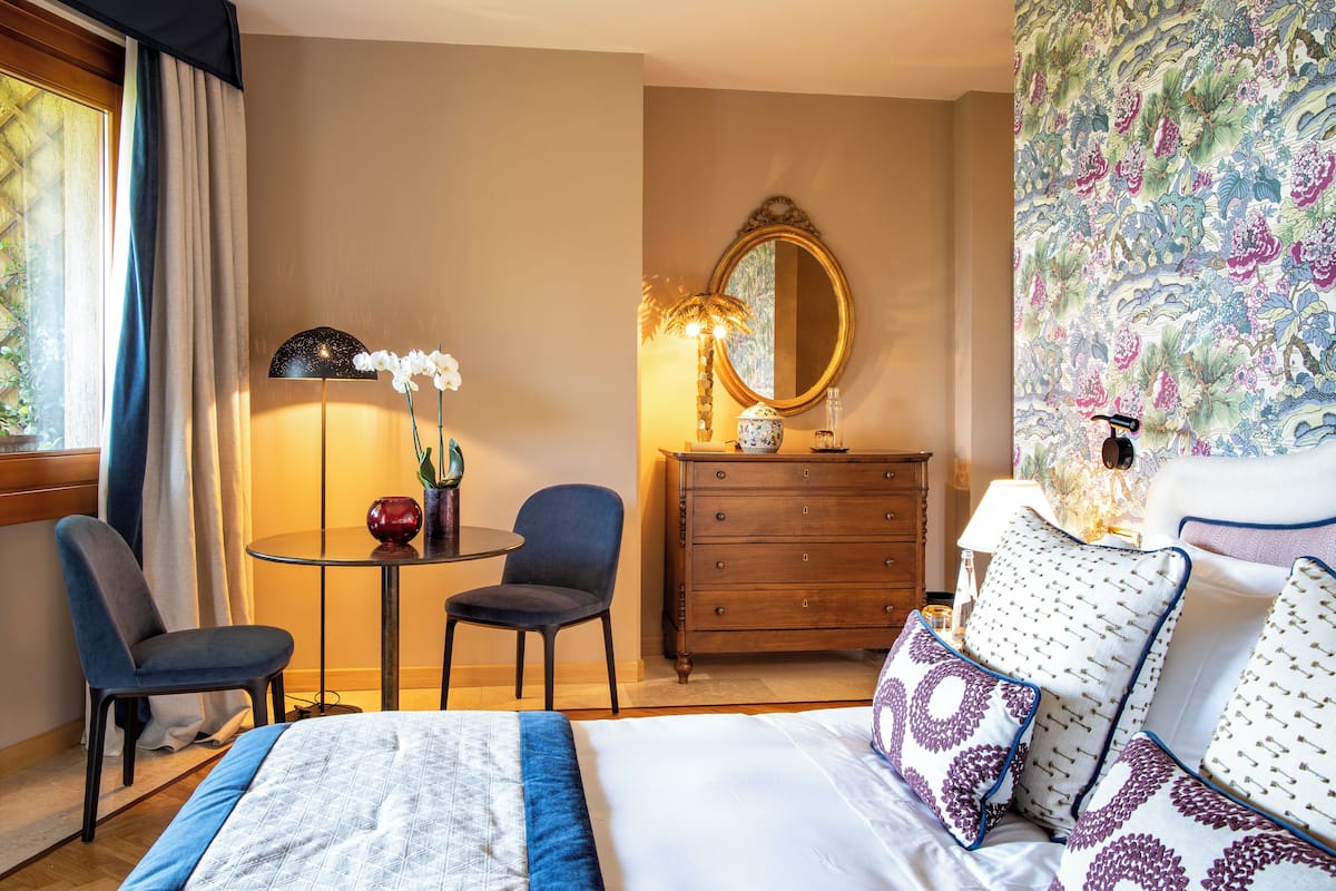 A hotel room with a bed, a desk, a chair, a dresser, and a mirror.