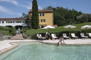 A pool area with lounge chairs and umbrellas, a pathway leading to a building, and a well-maintained lawn. - La Meridiana Relais & Chateaux (Garlenda)