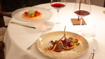 A dining table with two plates of food, two wine glasses, and cutlery.