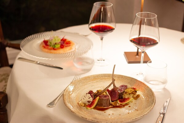 A dining table with two plates of food, two wine glasses, and cutlery. - La Meridiana Relais & Chateaux (Garlenda)