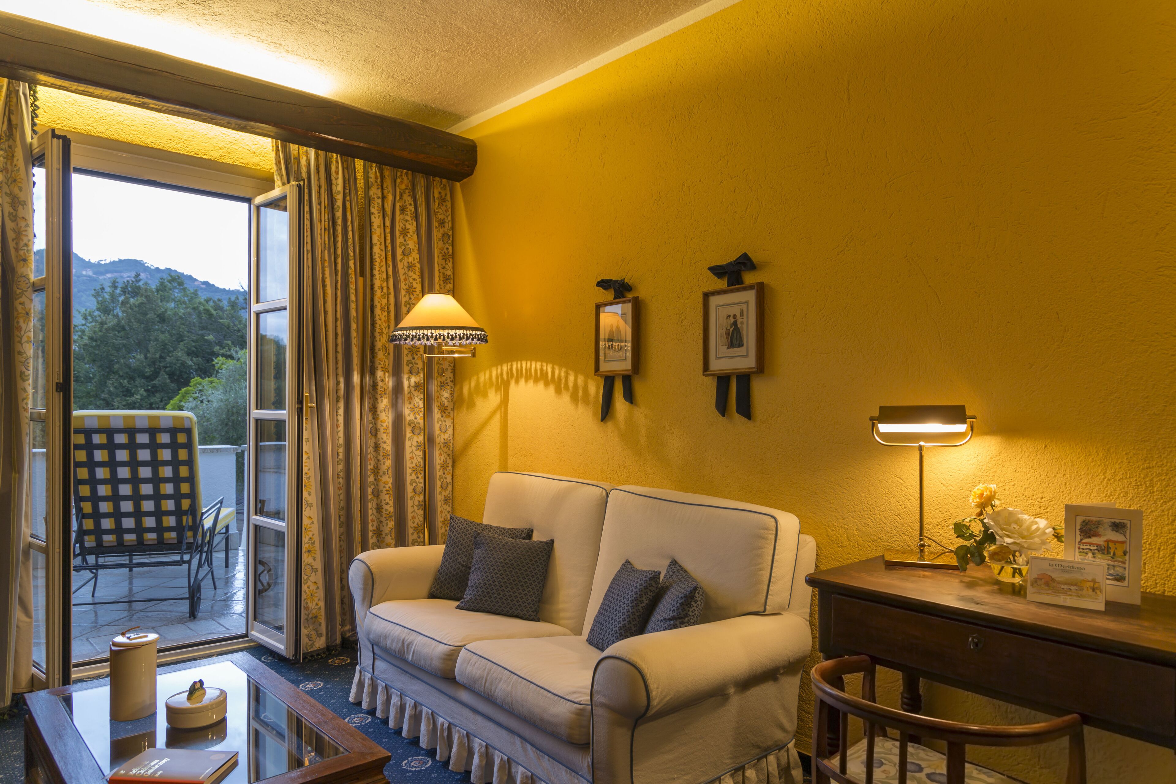 A room with a sofa, a desk, a lamp, and a view of the outdoors.