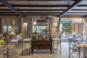 A restaurant with a rustic interior, featuring wooden beams, a central wooden bench, and a view of the outdoor patio area. - La Meridiana Relais & Chateaux (Garlenda)