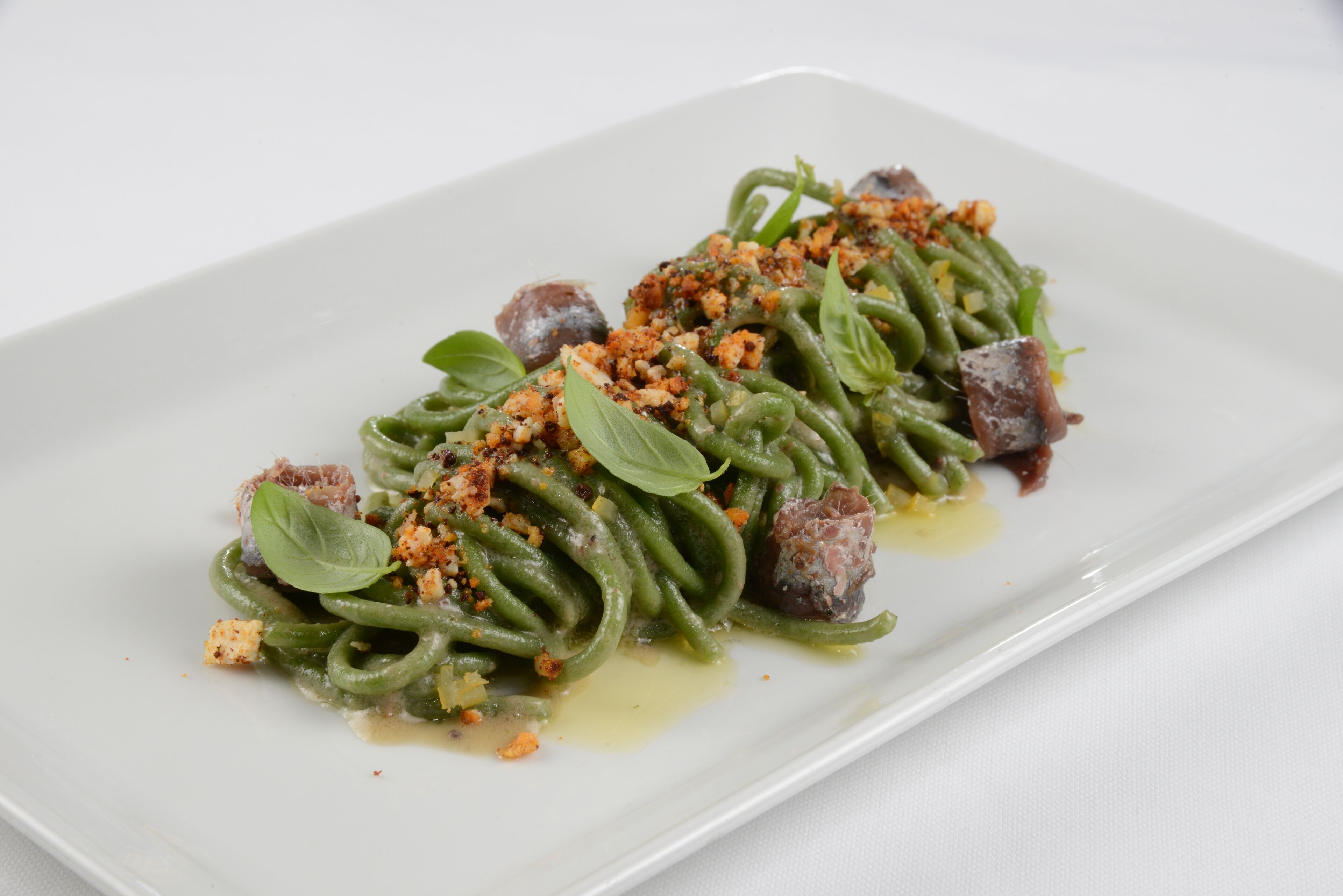Un plato de pasta con salsa verde, queso desmenuzado y hojas de albahaca.