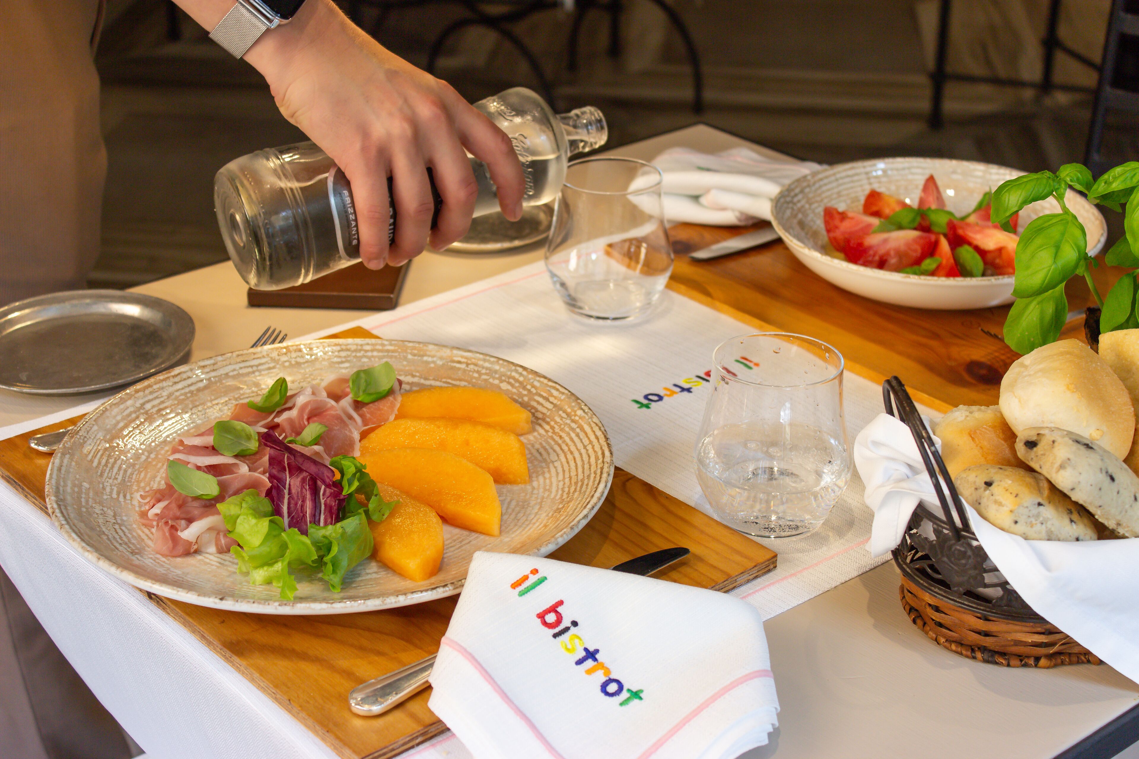 Una mesa servida con platos de comida, un vaso de agua y una cesta de pan.