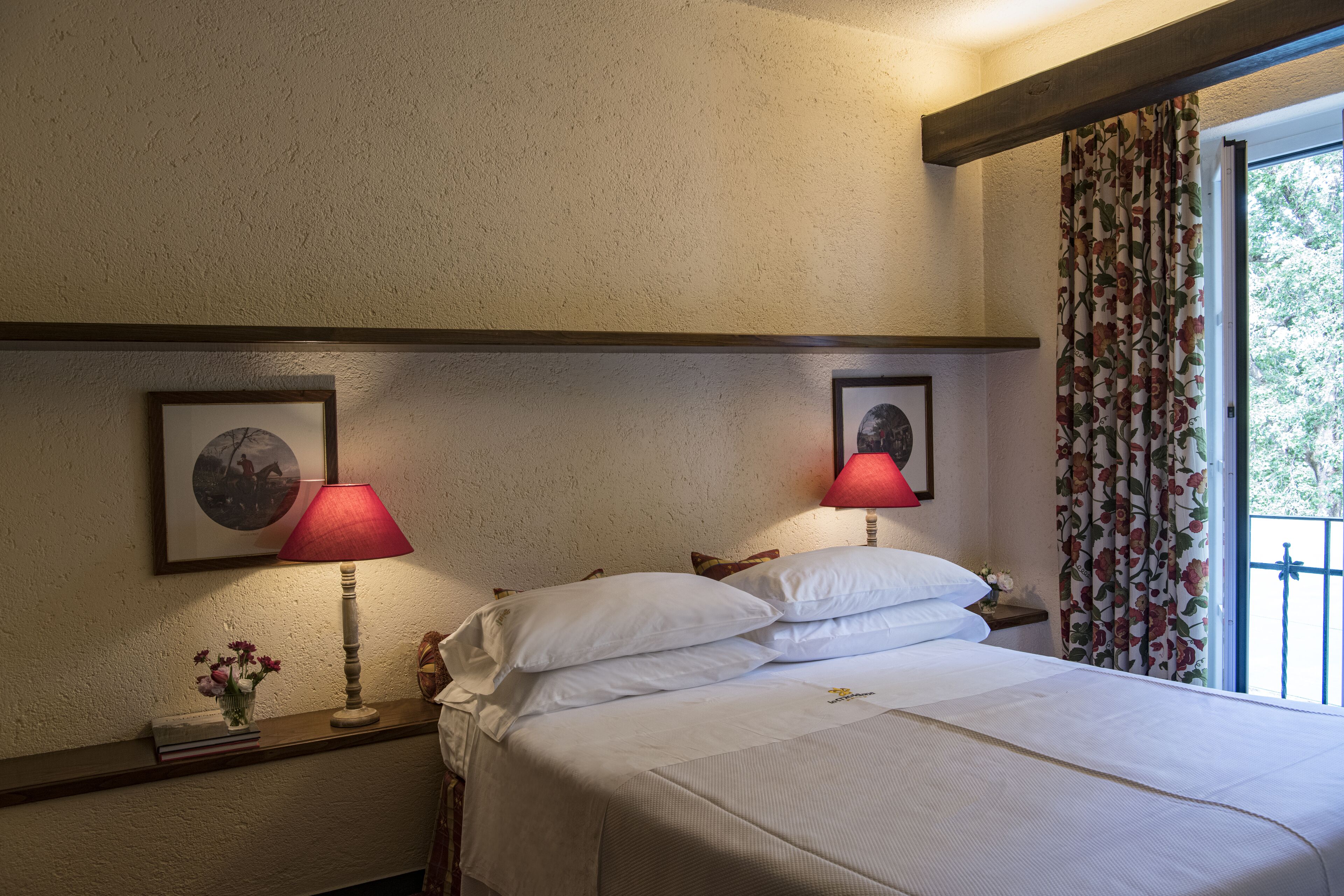 A neatly made bed with white linens, a vase with flowers, and two framed pictures on the wall.