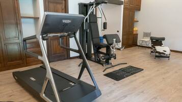 Gimnasio en casa con cinta de correr, máquina de pesas y sillas de ejercicio.