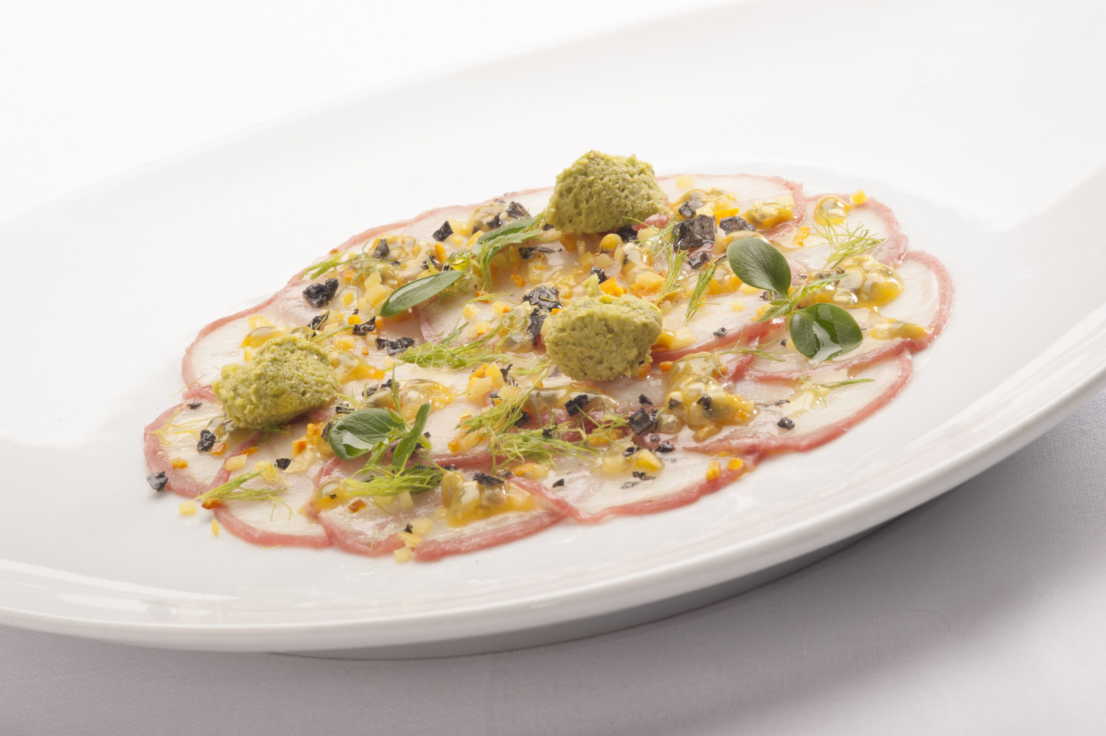 A white plate with a dish of thinly sliced meat, corn, and herbs.