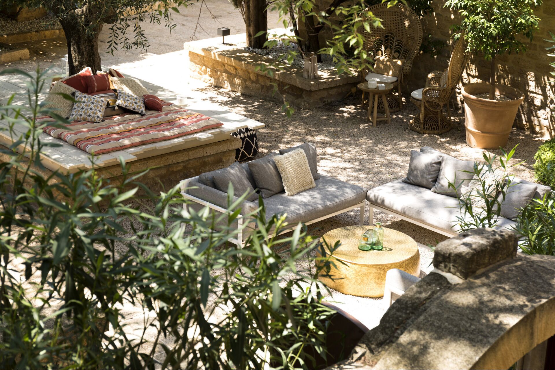 Un espace extérieur aménagé avec un canapé, des fauteuils et une table ronde, le tout entouré de plantes et d’arbres.