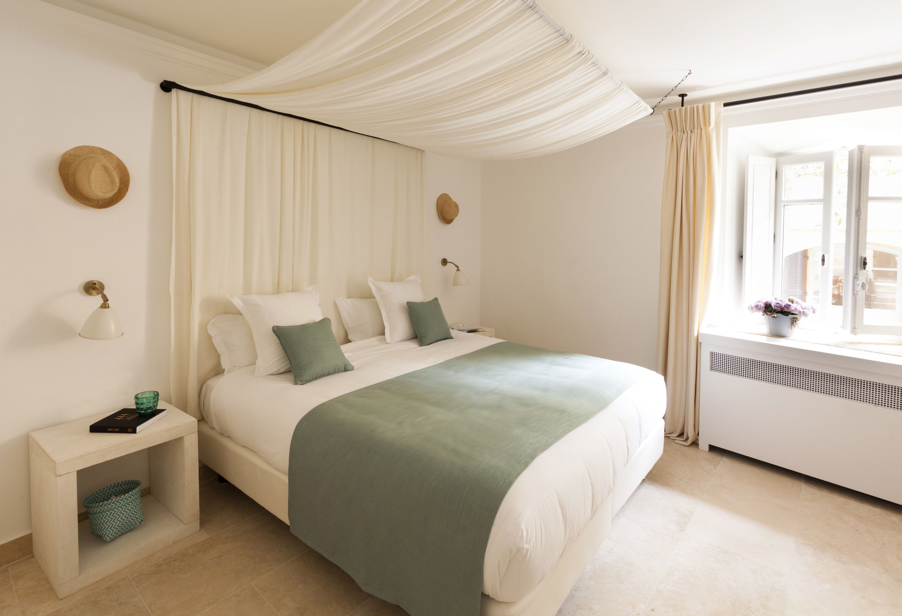 Un dormitorio ordenado con cama, mesitas de noche y una ventana con cortinas.