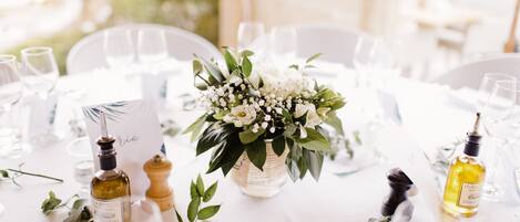 A table set for a wedding reception with a centerpiece of white flowers, two bottles of olive oil, and a menu card.