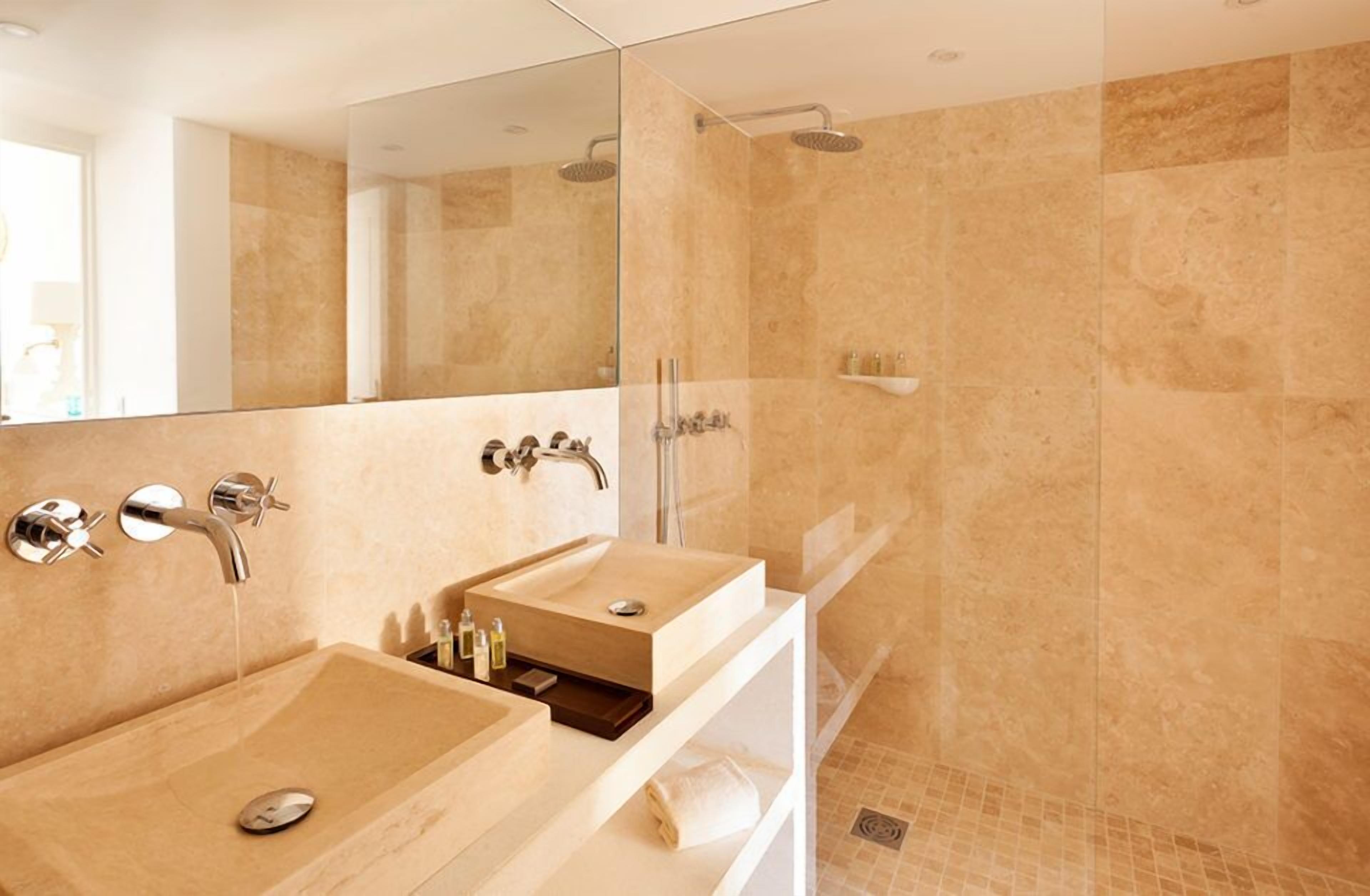 Een moderne badkamer met een grote spiegel, twee wastafels, een douche en een douchecabine met glazen wanden.