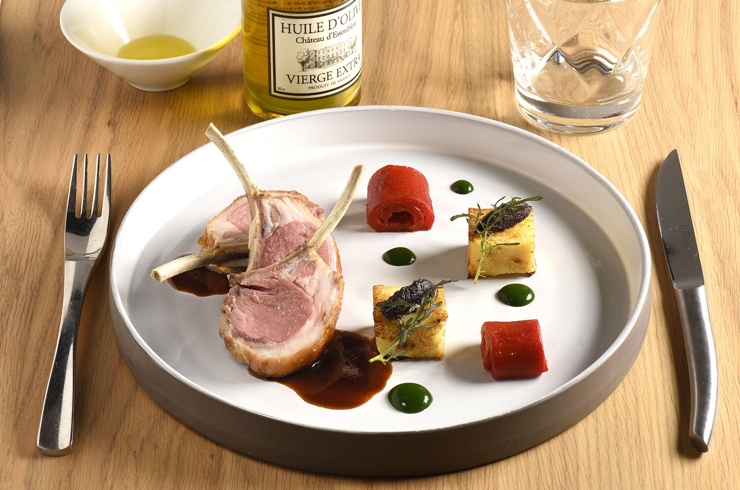 Un piatto di cibo con una bottiglia d'olio, un bicchiere d'acqua e posate su un tavolo di legno.