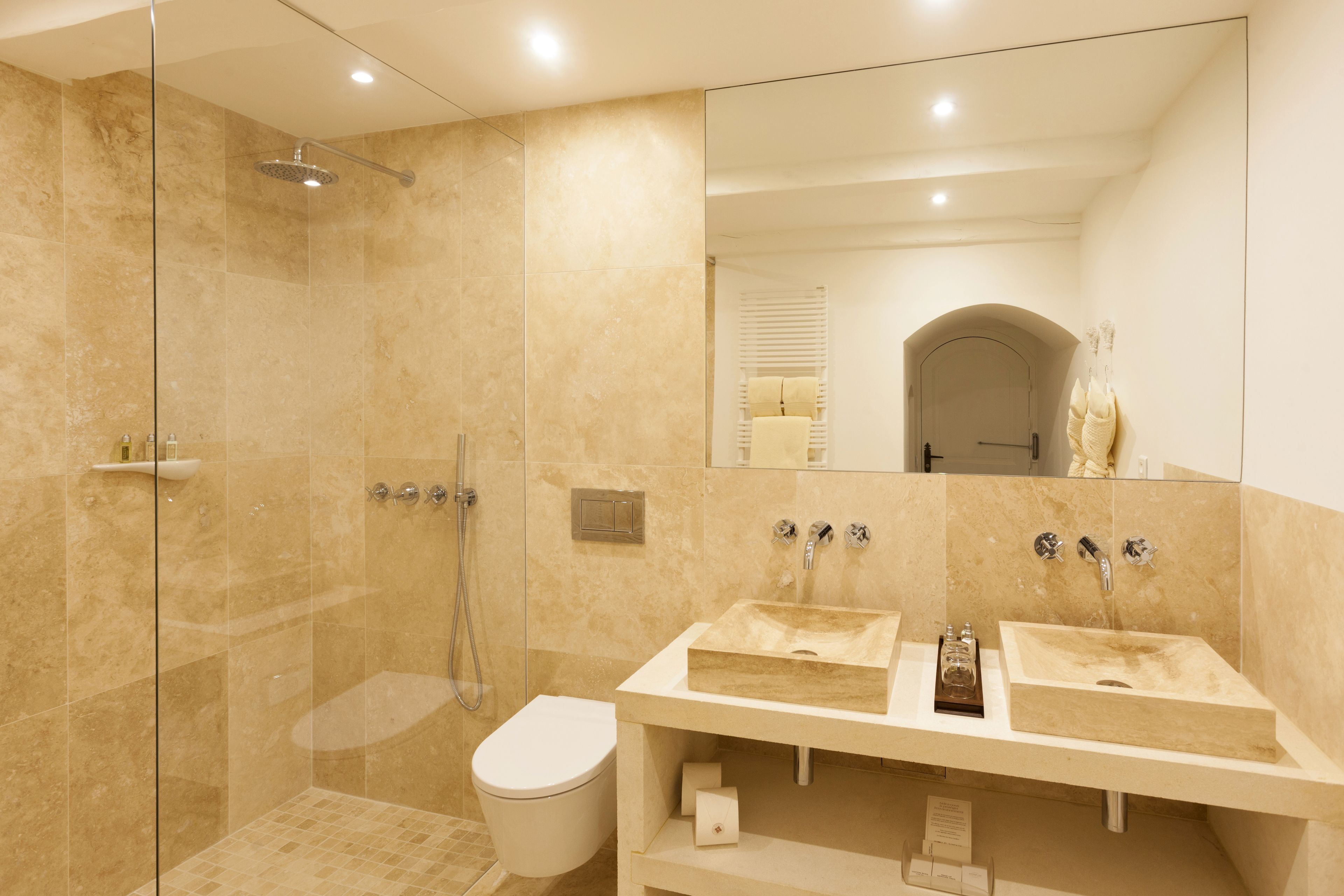 A modern bathroom with two sinks, a glass-enclosed shower, and a toilet.