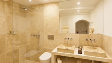 A modern bathroom with two sinks, a glass-enclosed shower, and a toilet.