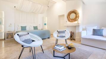 A modern living room with a sofa, two white wicker chairs, a coffee table, and a bed with a white canopy.