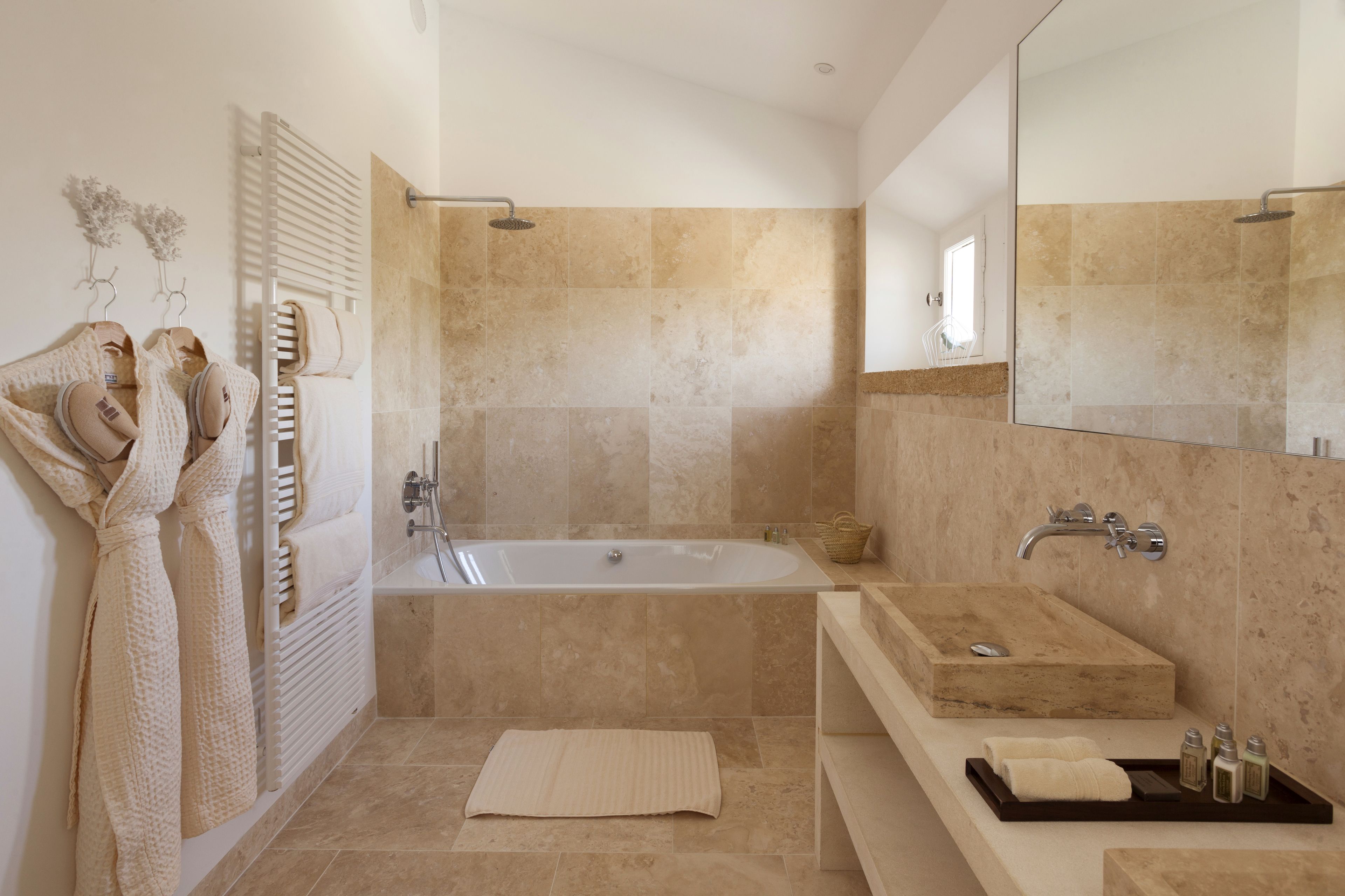 A modern bathroom with a bathtub, a large mirror, a vanity with a sink, and a towel rack with robes.