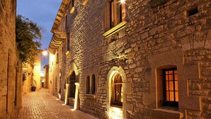 Una calle empedrada flanqueada por edificios históricos de piedra, con ventanas de arco y alumbrada con una luz cálida.