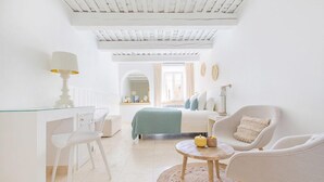Una habitación luminosa y blanca con una mesa de vidrio, un sofá y dos sillones.