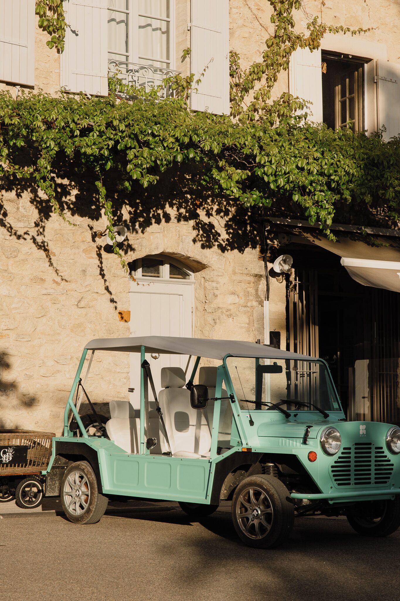 A turquoise vintage car parked in front of a stone building with white shutters and a white door.