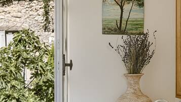 A bathroom with a large window, a vase with dried plants, and a painting of a tree on the wall.