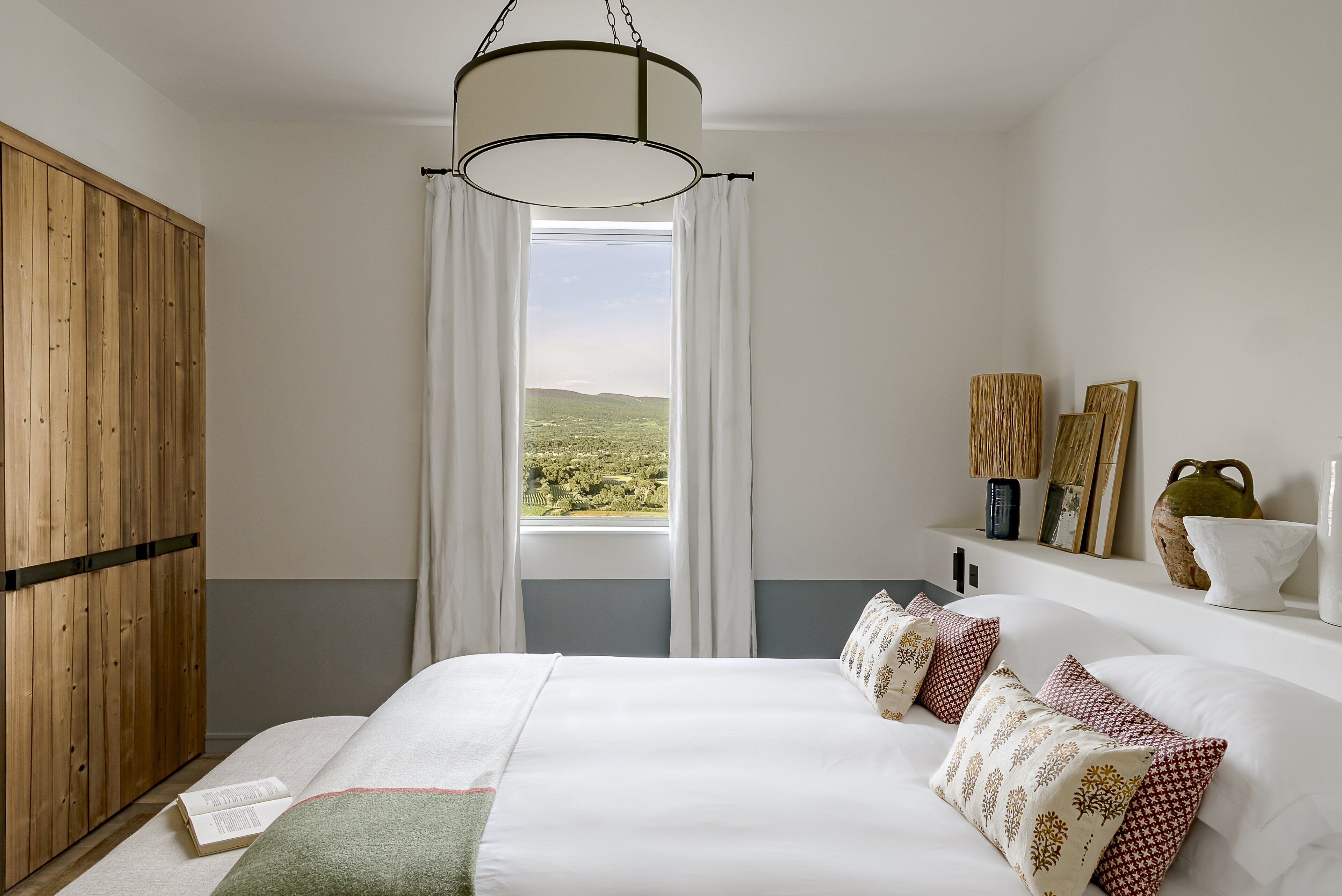 Una camera da letto con un letto grande, un armadio in legno, una finestra vista paesaggio e uno scaffale con oggetti decorativi.