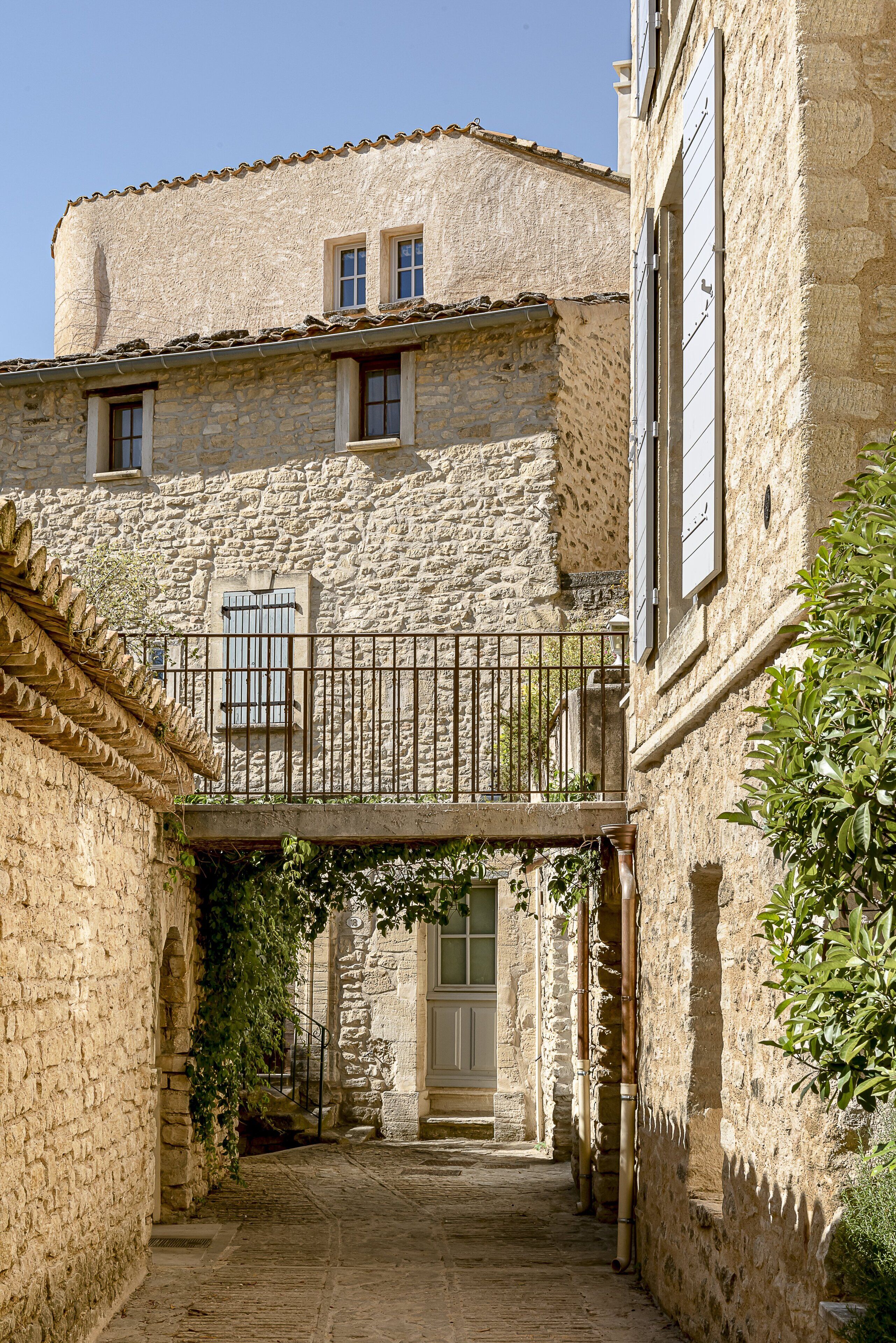 A narrow stone alleyway with a rustic building featuring a balcony with a metal railing.