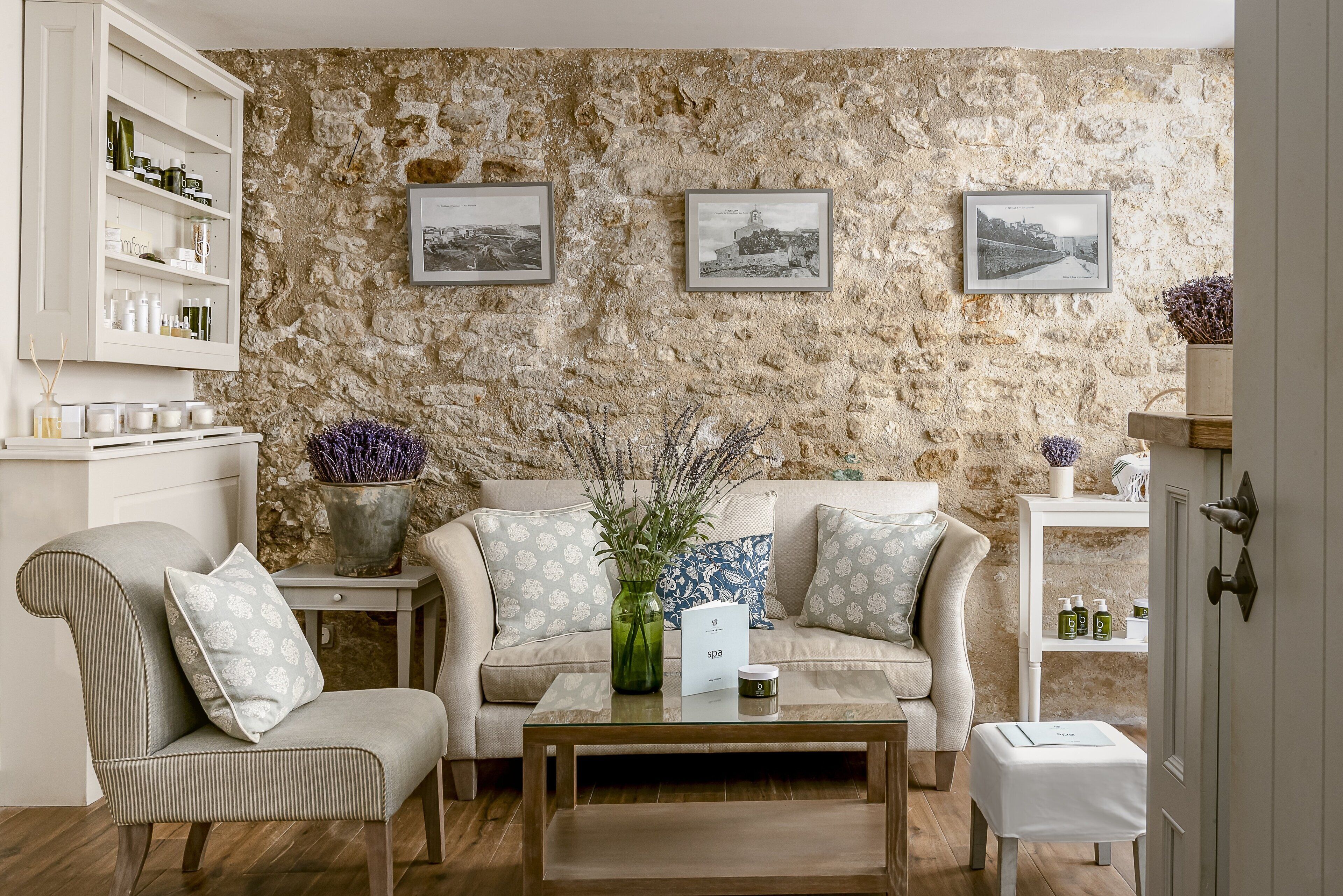 A cozy living room with a stone wall, a sofa, a chair, a coffee table, and a shelving unit with toiletries.