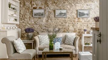 Un salon chaleureux avec un mur en pierre, un canapé, un fauteuil, une table basse et une étagère contenant des articles de toilette.