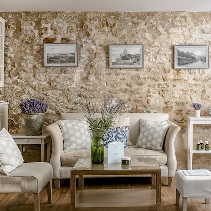 A cozy living room with a stone wall, a sofa, a chair, a coffee table, and a shelving unit with toiletries.