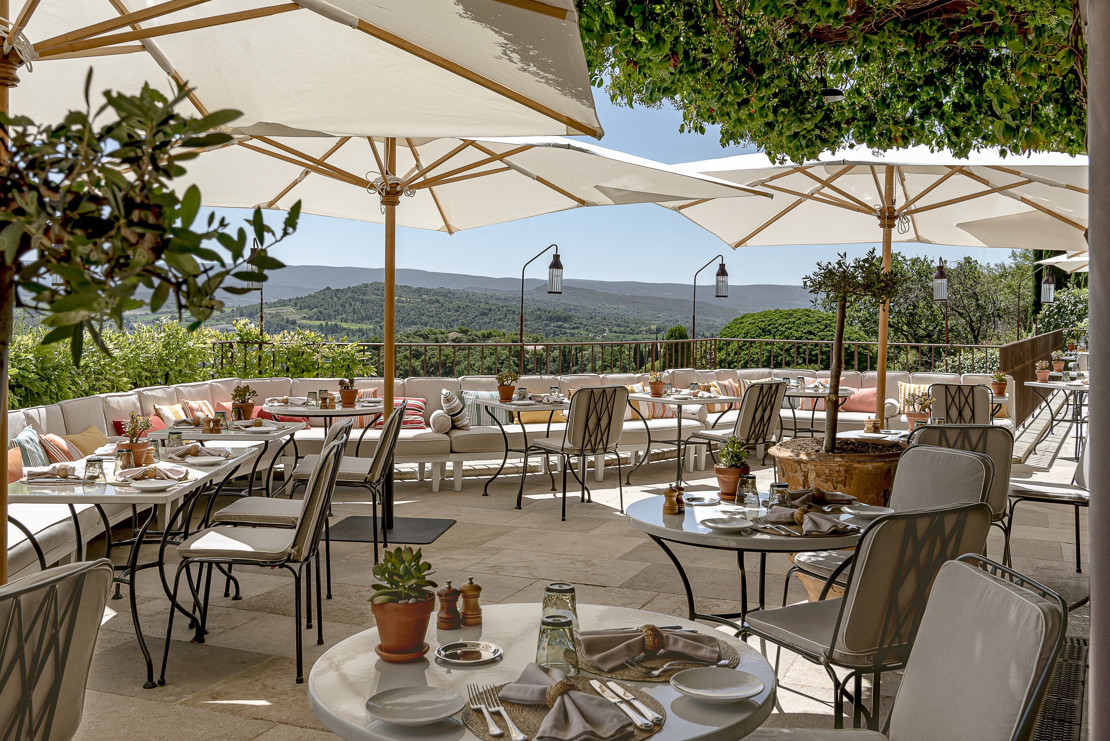 An outdoor patio with tables and chairs, umbrellas, and potted plants.