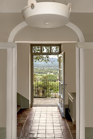A hallway leading to a balcony with a view of a green landscape.