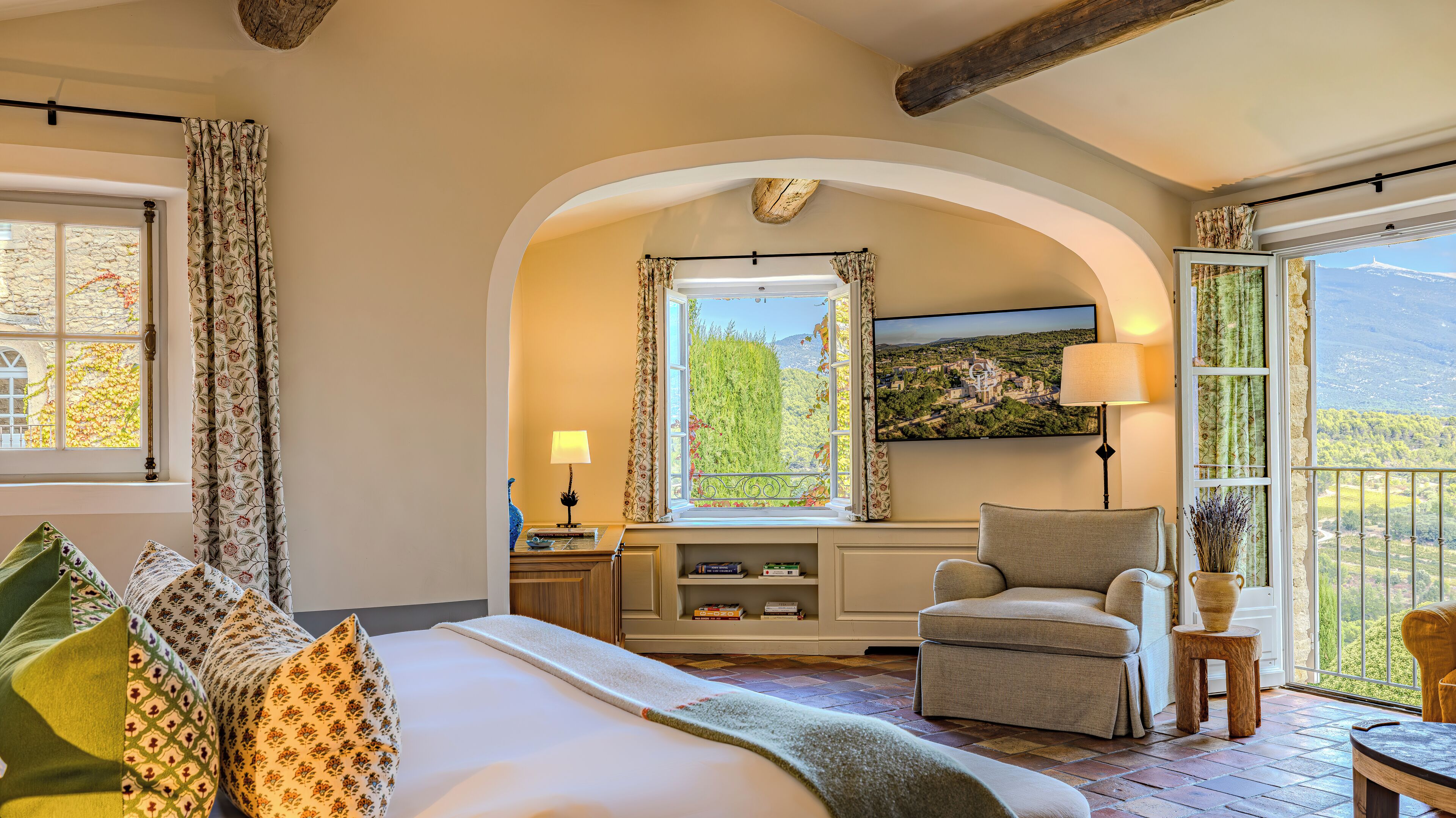 A bedroom with a large bed, a chair, a TV, and a window with a view of the countryside.