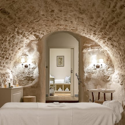A bedroom with a stone ceiling, a bed with white linens, and a small table with a lamp.