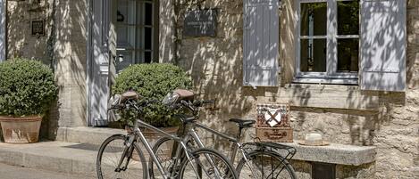 Un edificio de piedra con una puerta y ventanas blancas, bicicletas estacionadas al frente y una cesta en la pared.