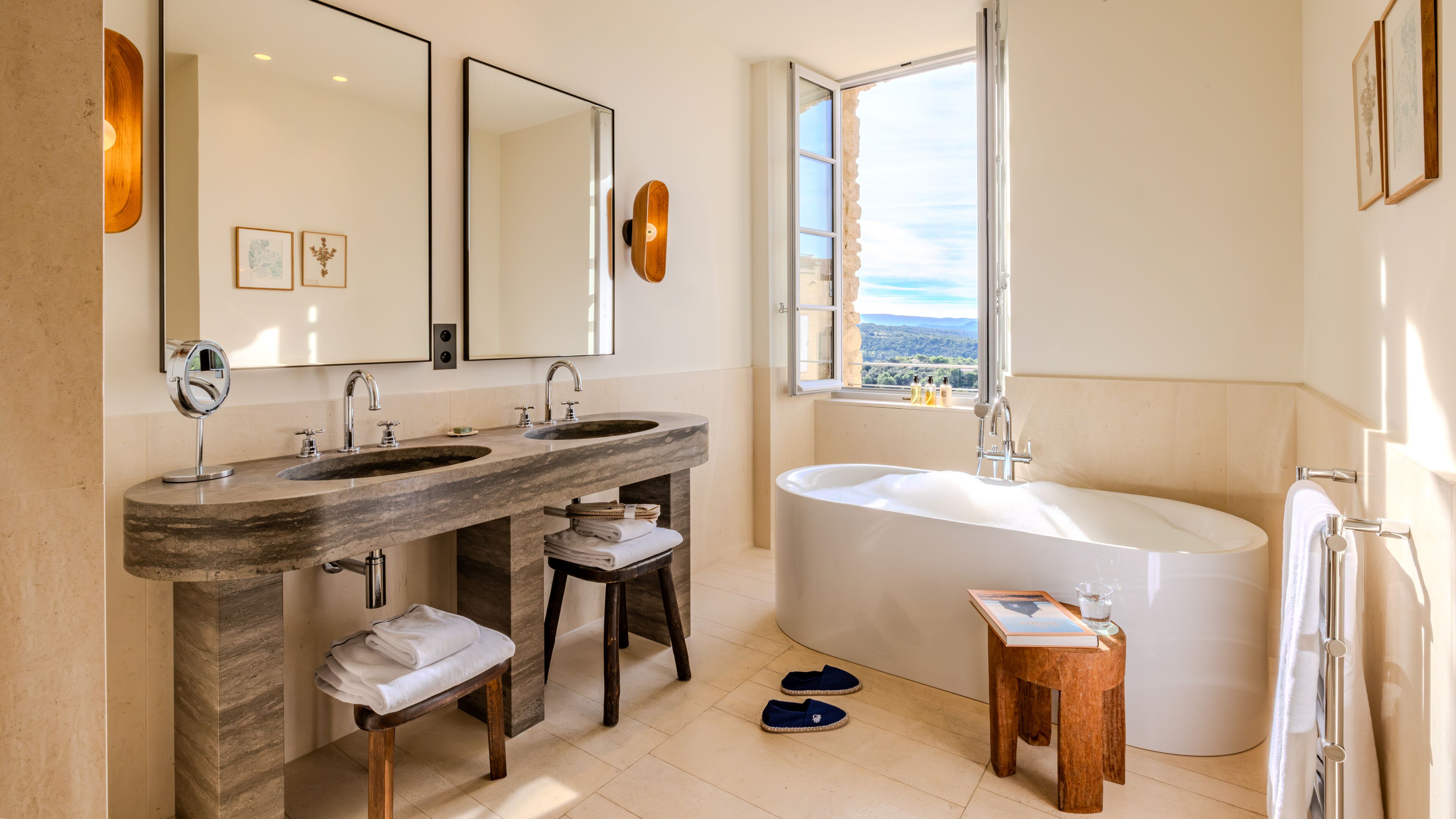 Une salle de bain avec deux lavabos, une grande baignoire, un meuble-lavabo avec un miroir et une fenêtre donnant sur un beau paysage.