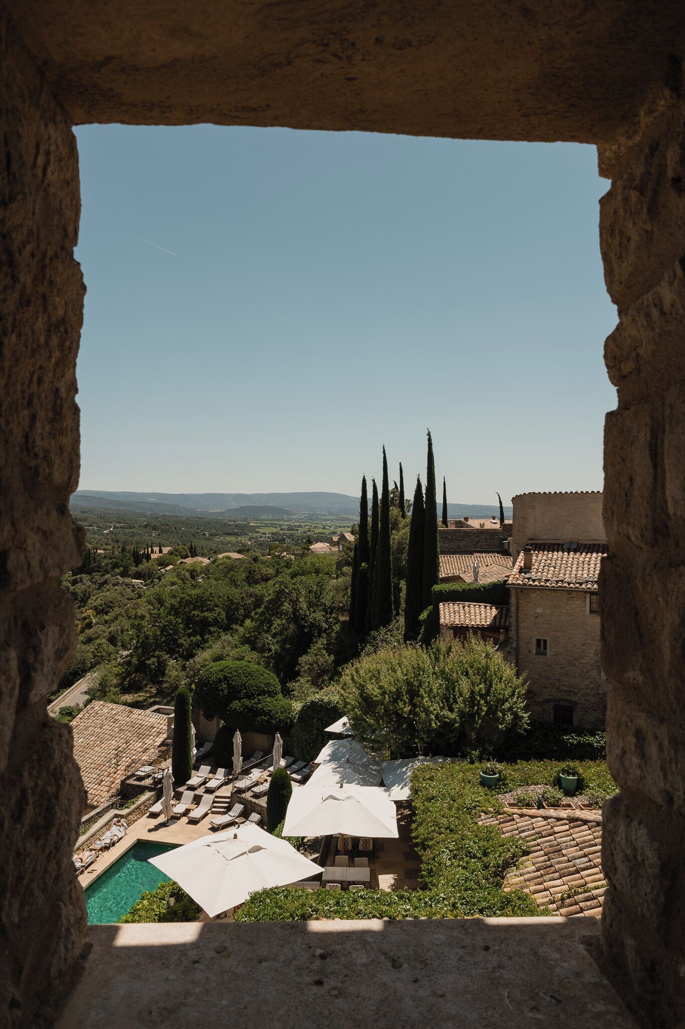 A view through an archway of a courtyard with a pool, lounge chairs, and a poolside area.
